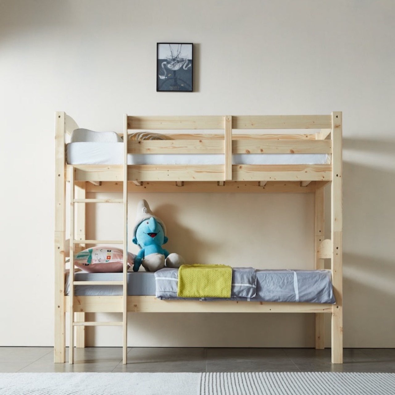 A single-over-single PineFlex bunk bed made of natural solid pine wood, with a ladder on the left side and a guardrail on the top bunk. The bed is set against a wall with a picture hanging above it, and a plush toy is seated on the lower bed.