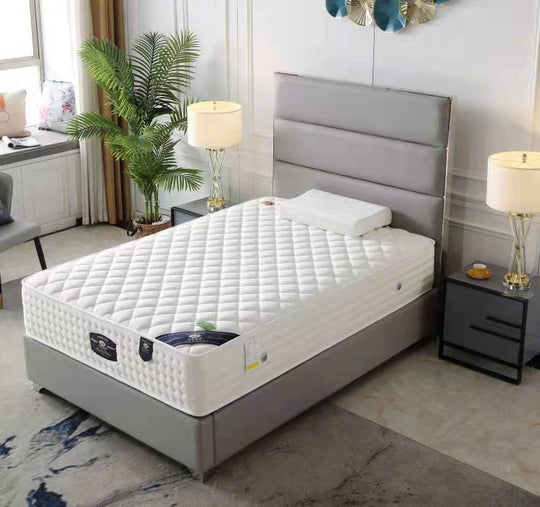 A white, patterned mattress on a gray bed frame, placed in a bedroom setting with decorative pillows, a nightstand, and a lamp.